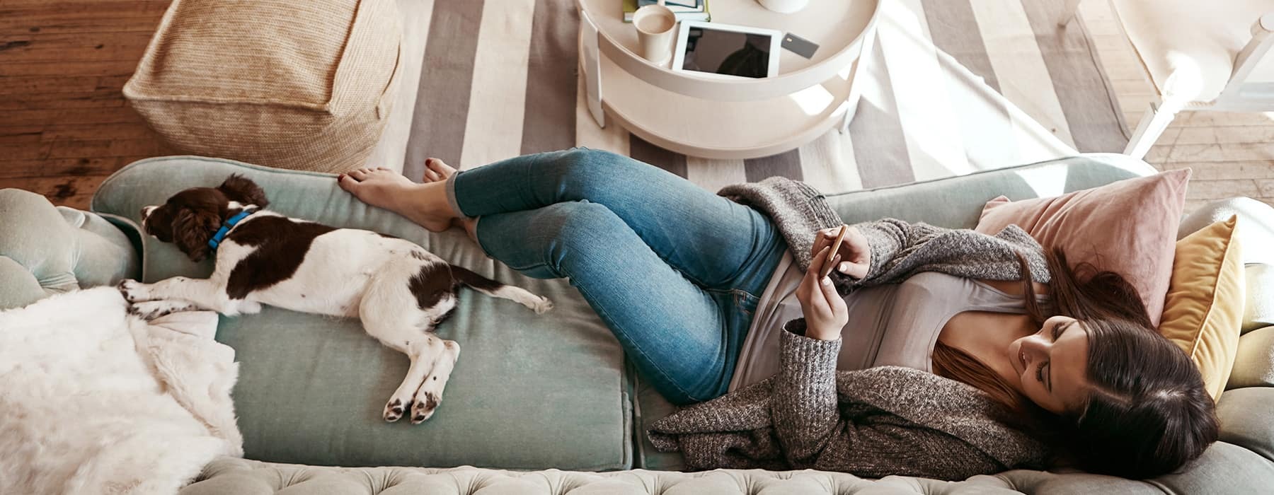 lifestyle image of a woman laying on a couch beside her puppy